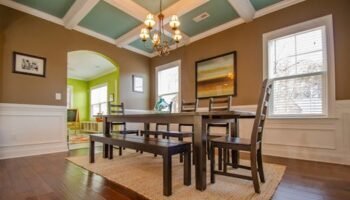 Stylish dining room featuring modern wood furniture, large windows, and artistic decor.