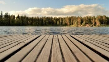 Serene wooden dock with a forested lake view under a bright summer sky in Sweden.
